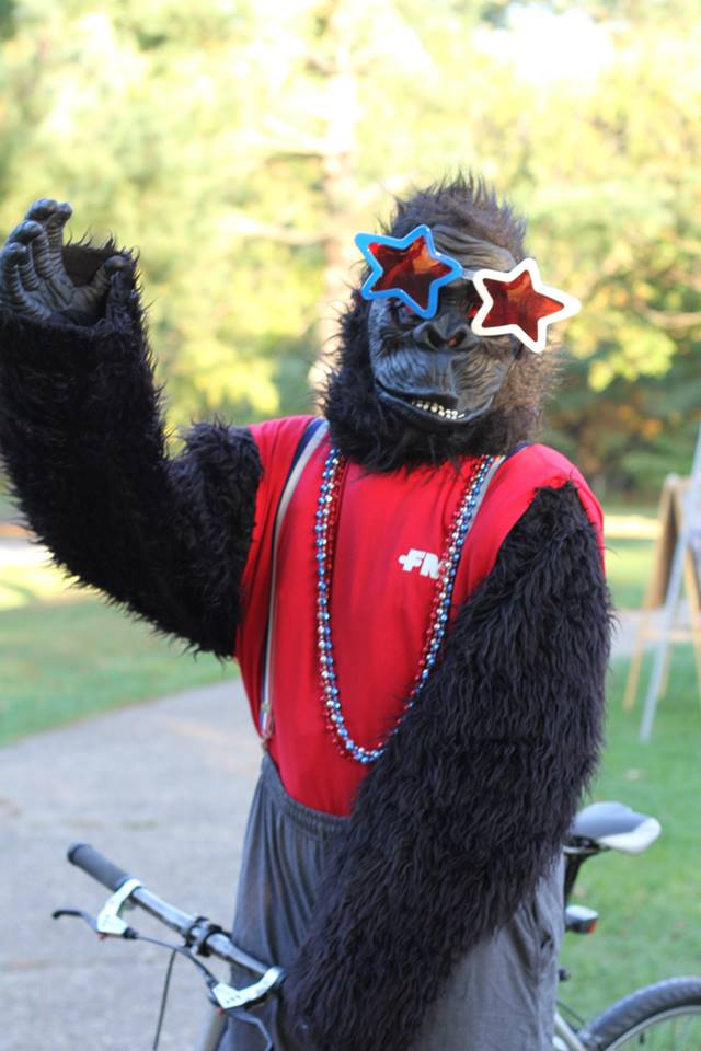 Person in gorilla costume wearing star-shaped glasses and red beads.