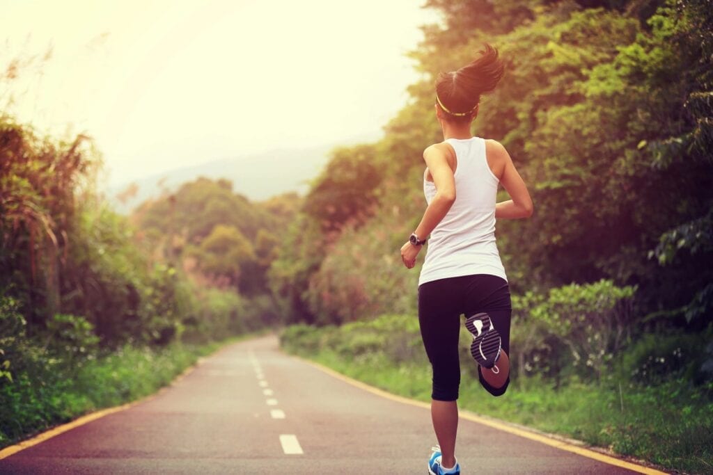 Woman jogging on a peaceful road surrounded by greenery.